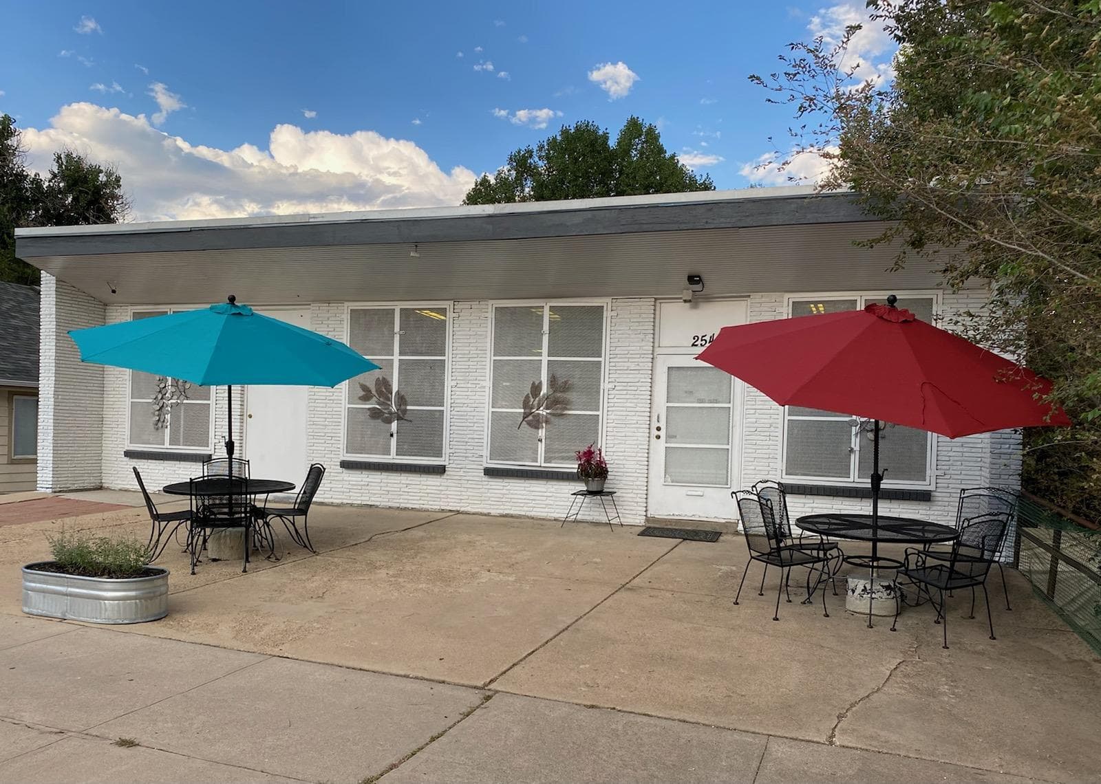 The Secular Hub building at 254 N. Knox Ct.: white brick, big gridded windows, and a teal and a red umbrella over patio tables