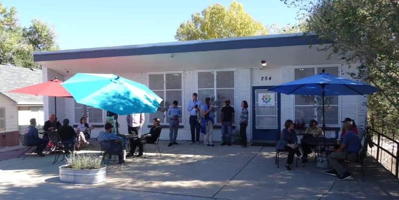 Members gathered on the patio at 254 Knox Ct. for Coffee & Community, under teal, red and blue umbrellas