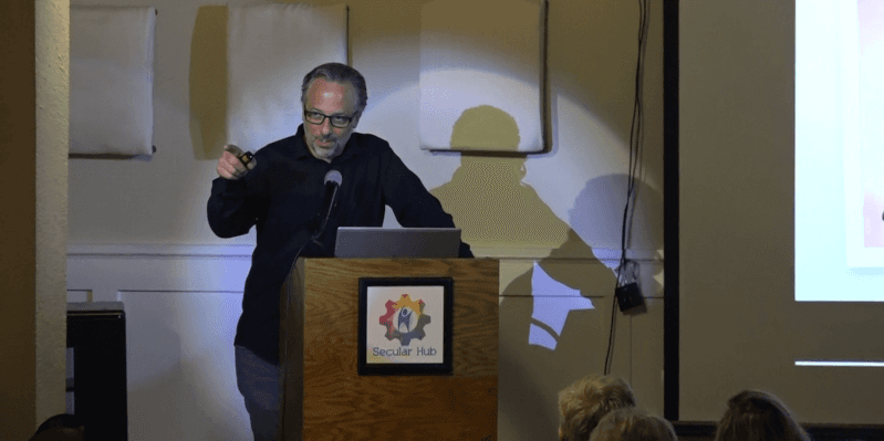 Seth Andrews speaking at a podium bearing the Secular Hub logo